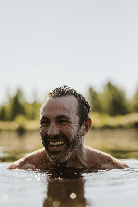older man swimming in river with head above water laughing